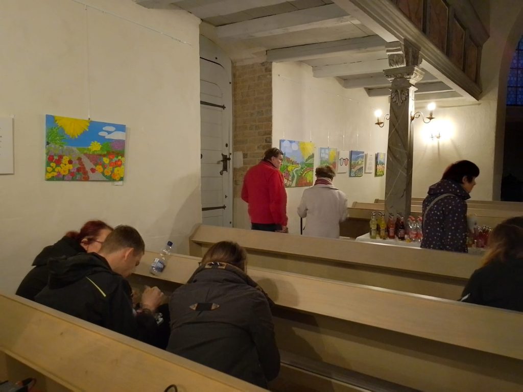 Gäste unterhalten sich, laufen herum, sitzen auf den Bänken und schauen sich die Bilder an