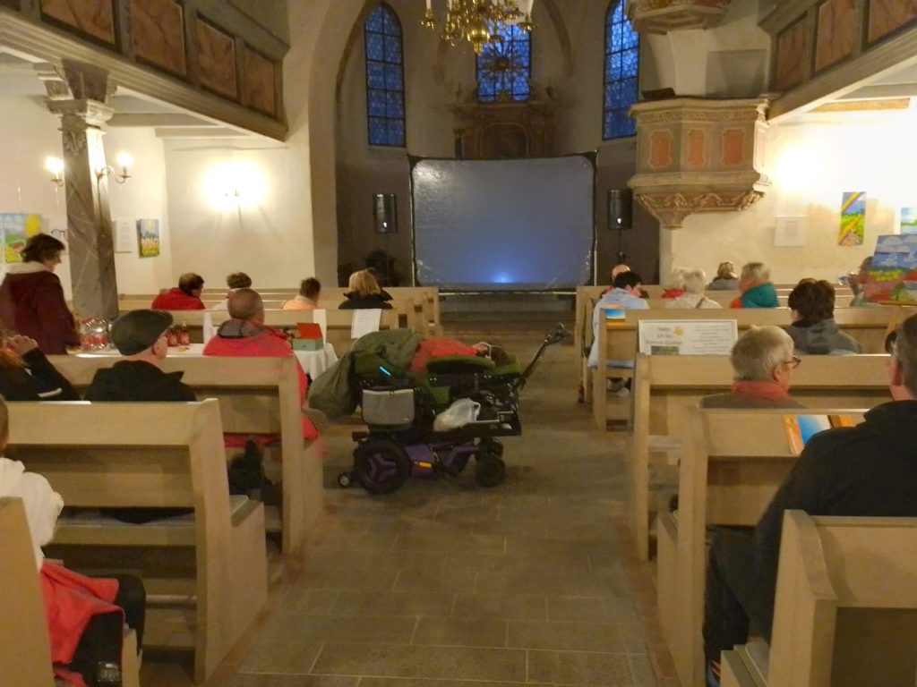 Einige Gäste sitzen auf den vorderen Kirchenbänken, bereit für den Filmabend